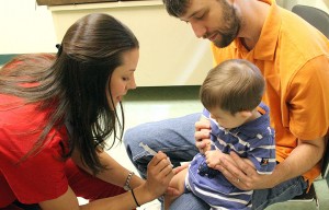 A nurse giving a vaccine to a young child being held by a parent.